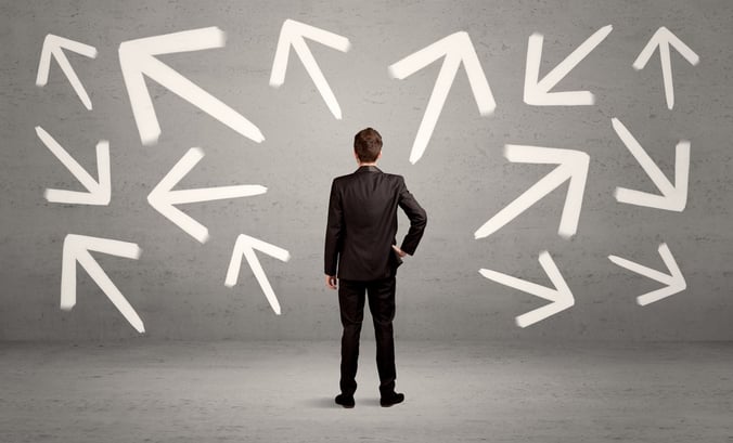 An elegant businessman standing with his back in front of urban wall full of arrows pointing in different directions concept